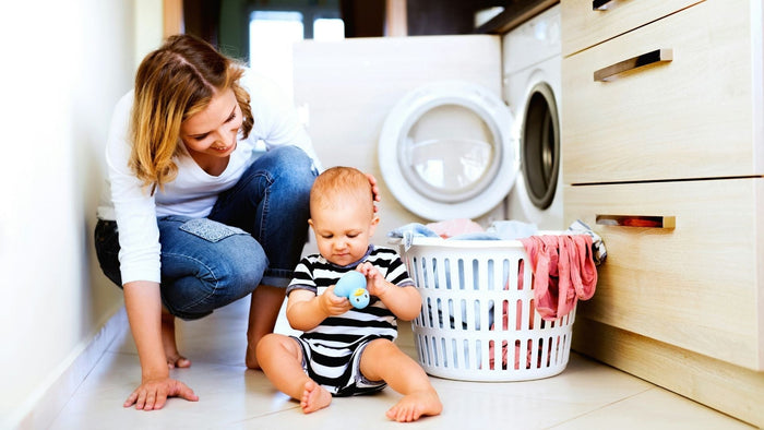 A mother and her baby in front of a washing basket and washing machine